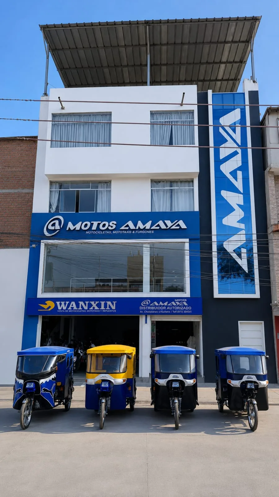 Fachada completa de Motos Amaya en Piura: edificio blanco y azul con el rótulo Motos Amaya, la torre AMAYA y cuatro mototaxis en la puerta